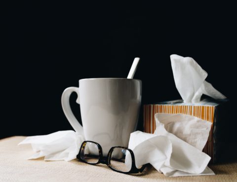 white mug on a table beside reading glasses and tissues