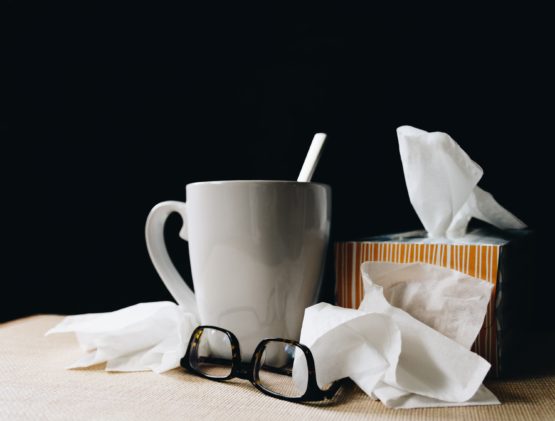 white mug on a table beside reading glasses and tissues