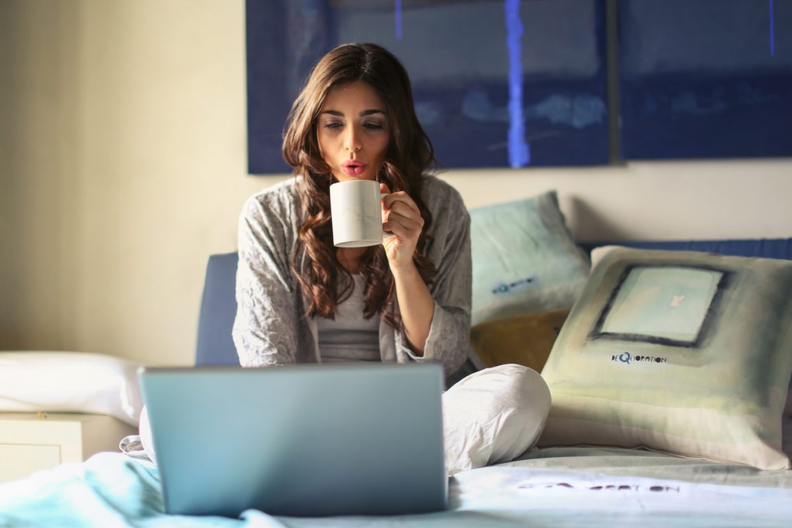woman in bed with laptop drinking tea